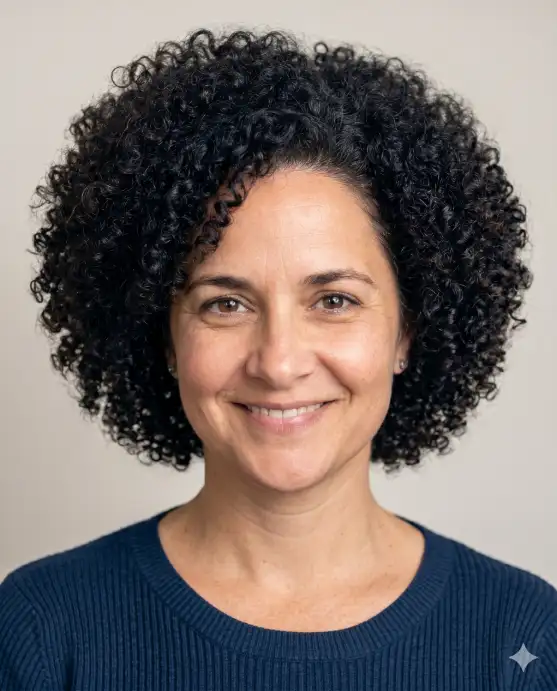 Create a realistic portrait using the uploaded photo, keeping the same face, eyes, and skin tone exactly. Change only the hairstyle to a full, natural curly afro with soft, defined coils and even volume all around. The color stays a deep natural black-brown. The person faces the camera with a warm, genuine smile. Shoot at eye level with bright, flattering lighting and a plain neutral background. Keep all facial features unchanged and the curl texture photorealistic. Use aspect ratio 4:5.