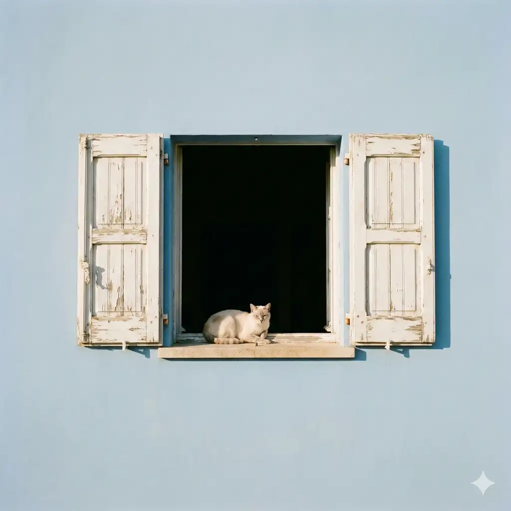 Create a minimalist architectural scene featuring a small cat resting on a sunlit windowsill. The window is centered in the frame and set into a smooth, pastel blue exterior wall. Weathered white wooden shutters are open on both sides, showing subtle signs of age. Inside the window opening is a deep, dark interior, creating strong contrast that naturally frames the cat. The cat is small and light-colored, positioned calmly with its front paws resting on the stone sill, looking outward with a relaxed, curious expression. Use aspect ratio 1:1.