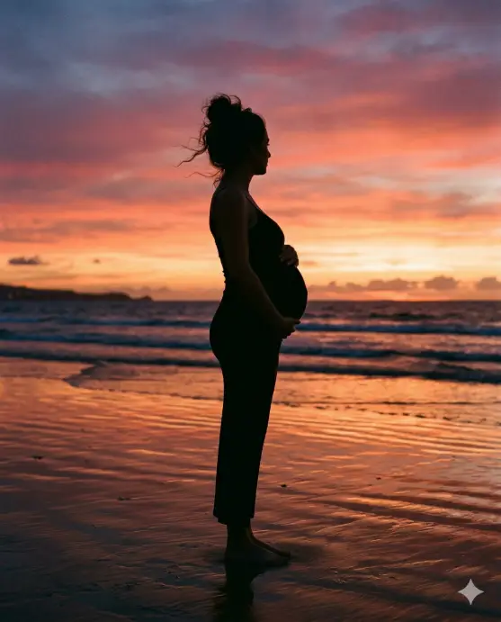 Create a silhouette photo of a pregnant woman standing on a quiet beach at sunset, turned sideways to clearly show her baby bump. She is wearing a form-fitting black maxi dress with thin spaghetti straps. One hand rests gently on top of her belly and the other hangs naturally at her side. Her hair is pulled up in a loose bun with a few strands blowing in the ocean breeze. The camera is at hip level, shooting straight on from the side. The sky behind her is a vivid gradient of deep orange, pink, and purple as the sun dips into the ocean horizon. The wet sand beneath her feet reflects the sky colors. Dark, dramatic silhouette with rich warm tones. Shot with a 50mm lens, deep depth of field. Use aspect ratio 4:5.