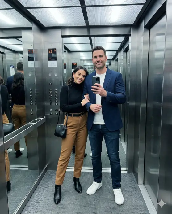 Create a realistic couple mirror selfie taken inside a modern elevator with mirrored walls. The man is wearing a tailored navy blazer over a white crew neck t-shirt with dark jeans and clean white sneakers. The woman is wearing a fitted black turtleneck tucked into high-waisted camel trousers with pointed ankle boots and a small leather handbag on her shoulder. He is holding the phone at chest level while she leans into his side with one arm linked through his. Both have calm, confident expressions with a slight smirk. The elevator interior has brushed steel walls, a mirrored ceiling reflection, and cool fluorescent panel lighting. The image has a sharp, clean, slightly cool-toned urban feel. Use aspect ratio 4:5.