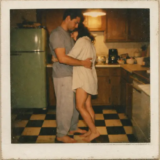 Create a vintage Polaroid photograph of a young couple slow dancing barefoot in a small kitchen with warm yellow overhead light. The man is wearing a plain gray t-shirt and sweatpants, and the woman is wearing an oversized button-down shirt that falls to her mid-thigh. His hands are on her waist and her arms are around his neck, with her head resting on his chest. Their eyes are closed. The kitchen has retro details like a green fridge, wooden cabinets, and a checkered floor. Soft warm tungsten lighting, heavy film grain, faded muted colors, slightly blurry like the camera was handheld. Shot on Polaroid SX-70 film. Use aspect ratio 1:1.