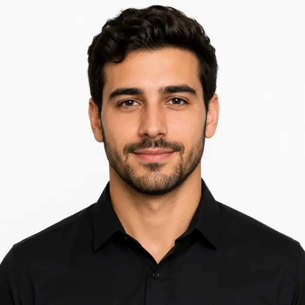 Create a minimalist studio headshot of a person against a smooth solid white backdrop. They are wearing a simple black collared shirt, standing straight on with a calm and confident expression. Their posture is upright with squared shoulders and a slight natural smile. The camera is at eye level with a head-and-shoulders crop. Even, professional studio lighting with soft shadows. The mood is clean, modern, and sharp. Use aspect ratio 1:1.