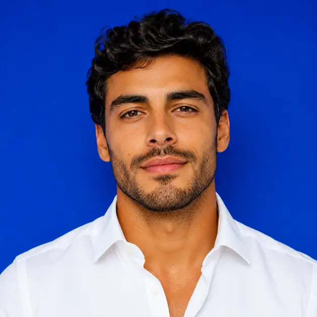 Create a close-up portrait of a person looking directly into the camera with a relaxed, confident expression and squared shoulders. They are wearing a bright white shirt. The camera is at eye level with a tight crop on the face and upper chest. The background is a solid vivid cobalt blue wall. Use even, punchy lighting with strong color contrast. The tones are rich and saturated. Use aspect ratio 1:1.