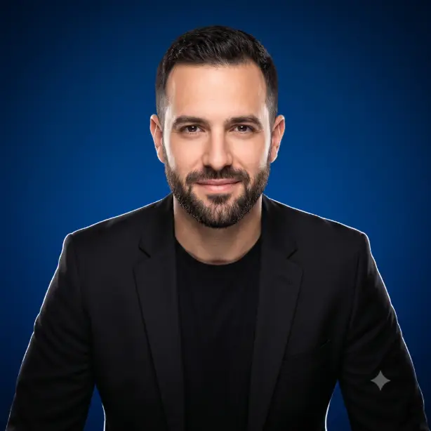 Create a bold studio headshot of the person in the uploaded photo, preserving their exact features. They are wearing a fitted black blazer over a black t-shirt, shoulders squared with a slight forward lean and a self-assured, closed-mouth smile. Shoot at eye level from the shoulders up. Crisp, even beauty lighting from the front with a subtle rim light separating them from the background. The background is a smooth, deep royal blue studio backdrop with a gentle vignette. Sharp, modern editorial style with strong color contrast. Use aspect ratio 1:1.