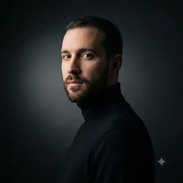 Create a moody professional portrait of the person in the uploaded photo, keeping their face unchanged. They are wearing an all-black outfit with a fine-knit black turtleneck, body angled three-quarters away with face turned back to the camera and a calm, penetrating gaze. Shoot at eye level, tightly framed from the shoulders up. Low-key dramatic lighting from one side, leaving the far side of the face in soft shadow. The background is near-black charcoal with a faint gradient of light behind the head. Cinematic fine art portrait style with deep shadows and muted contrast. Use aspect ratio 1:1.