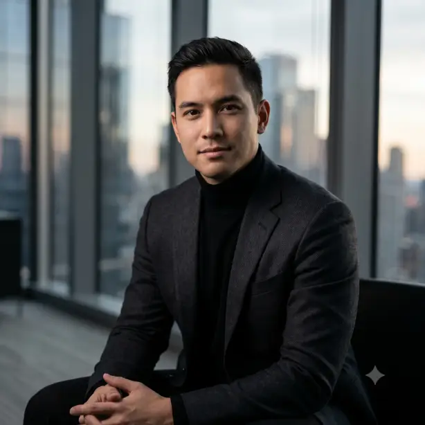 Create an executive portrait of the person in the uploaded photo, preserving their exact likeness. They are wearing a structured dark blazer over a black turtleneck, seated slightly angled with hands loosely clasped and a calm, assured expression looking straight into the lens. Shoot at eye level from the chest up. Dramatic soft window light from the right creating gentle shadow definition on one side of the face. The background shows a blurred high-rise office interior with floor-to-ceiling windows and a city skyline in soft bokeh. Refined editorial portrait style with muted, cinematic tones. Use aspect ratio 1:1.